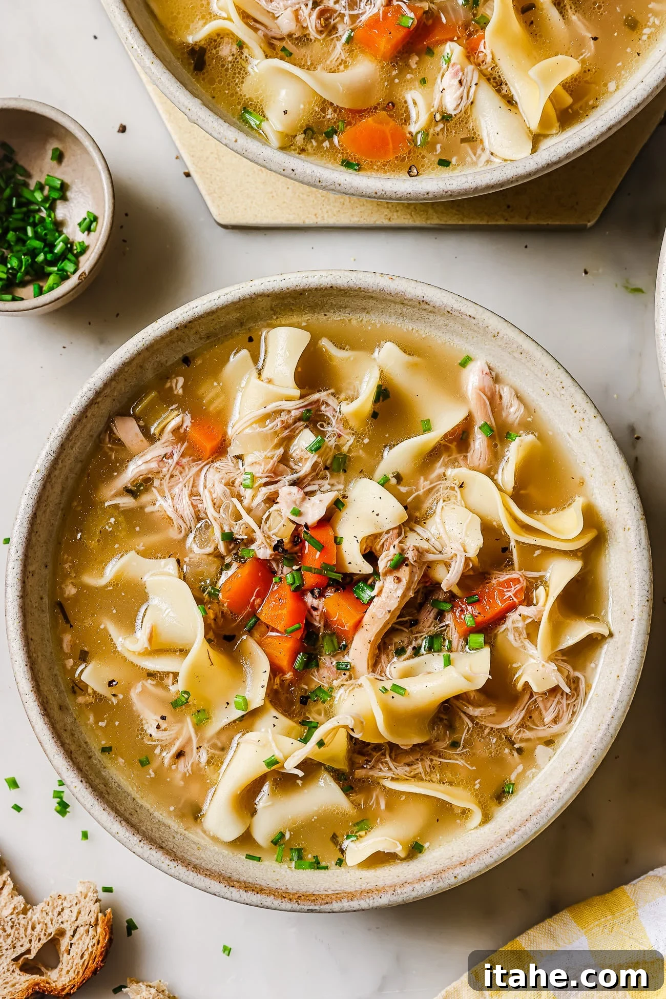 A bowl of slow cooker chicken noodles garnished with chives, ready to be enjoyed.