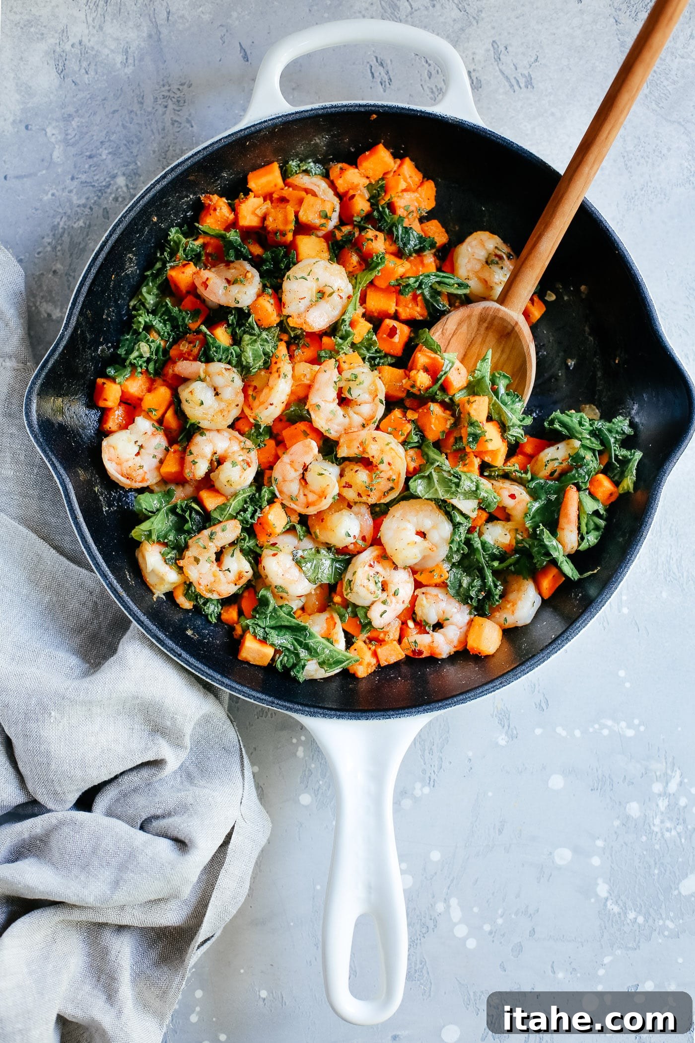 overhead view of a white skillet containing shrimp, sweet potato and kale