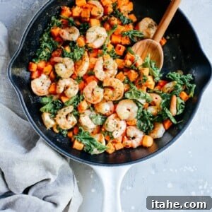 overhead view of a white skillet containing shrimp, sweet potato and kale