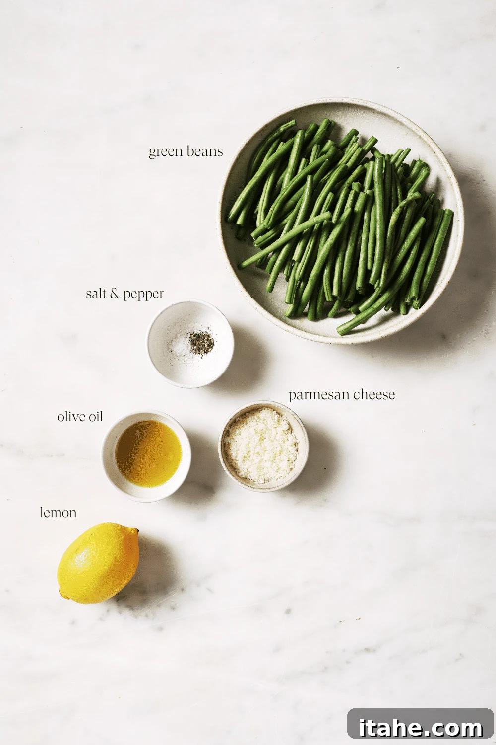 Perfectly Crispy Air Fryer Green Beans 3 Small bowls of pre-measured ingredients including fresh green beans, olive oil, salt and pepper, grated Parmesan, and lemon wedges.