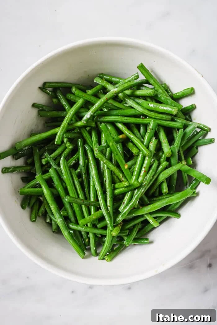 Perfectly Crispy Air Fryer Green Beans 4 Cleaned and trimmed green beans tossed in a bowl with olive oil, salt, and pepper.