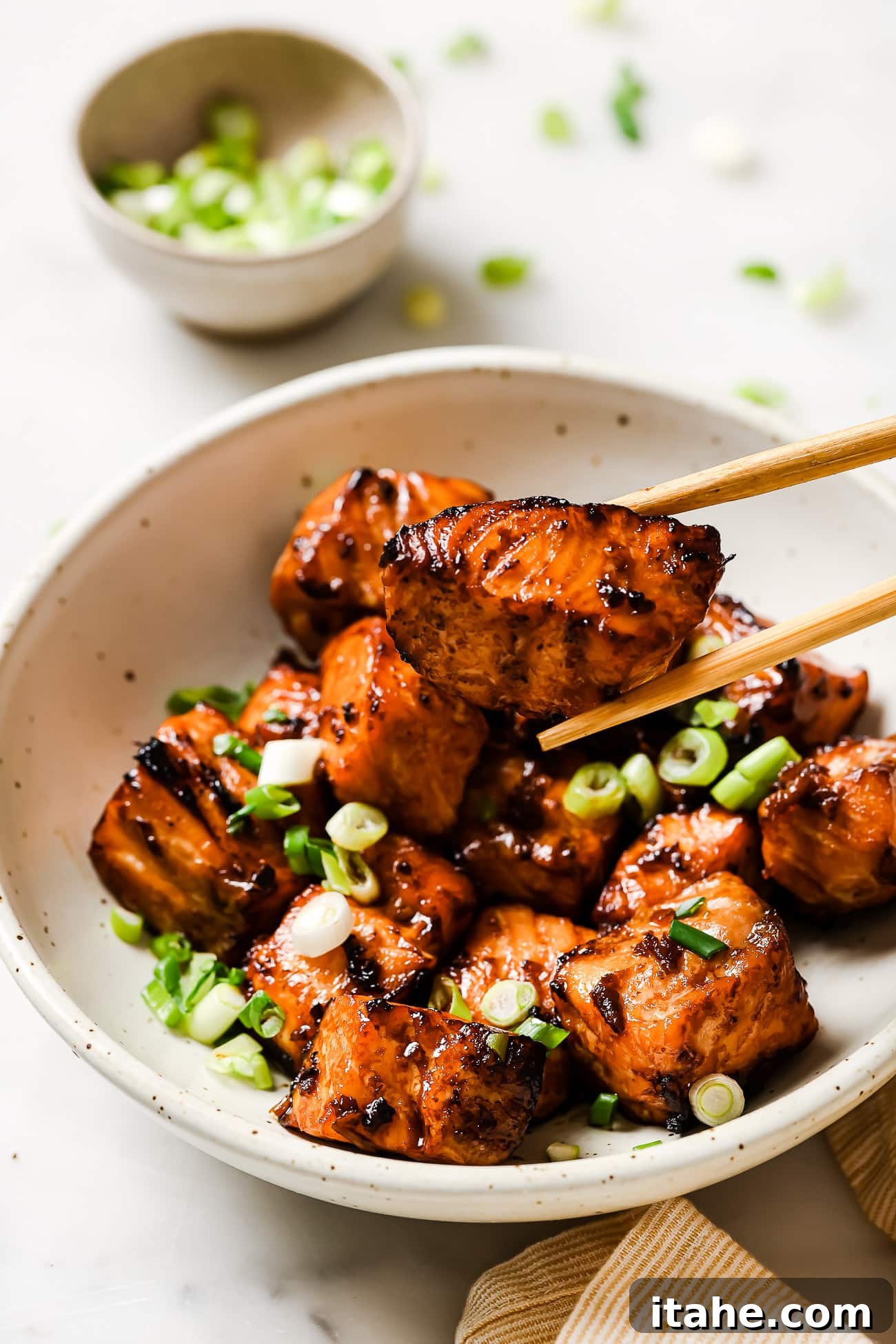 Golden Air Fryer Salmon Bites 7 Chopsticks picking up an air fryer salmon bite out of a bowl garnished with green onions and sesame seeds.