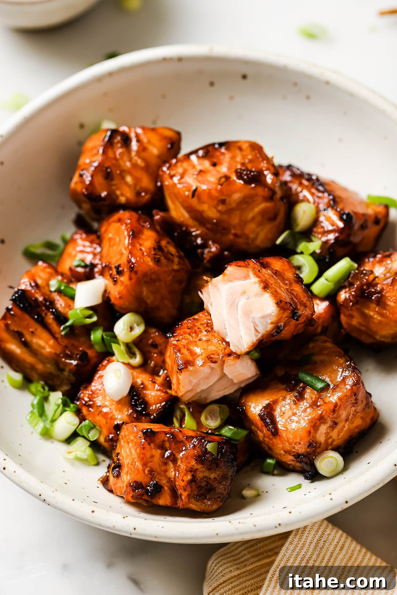 Golden Air Fryer Salmon Bites 8 Salmon bites in a bowl garnished with green onions and sesame seeds.