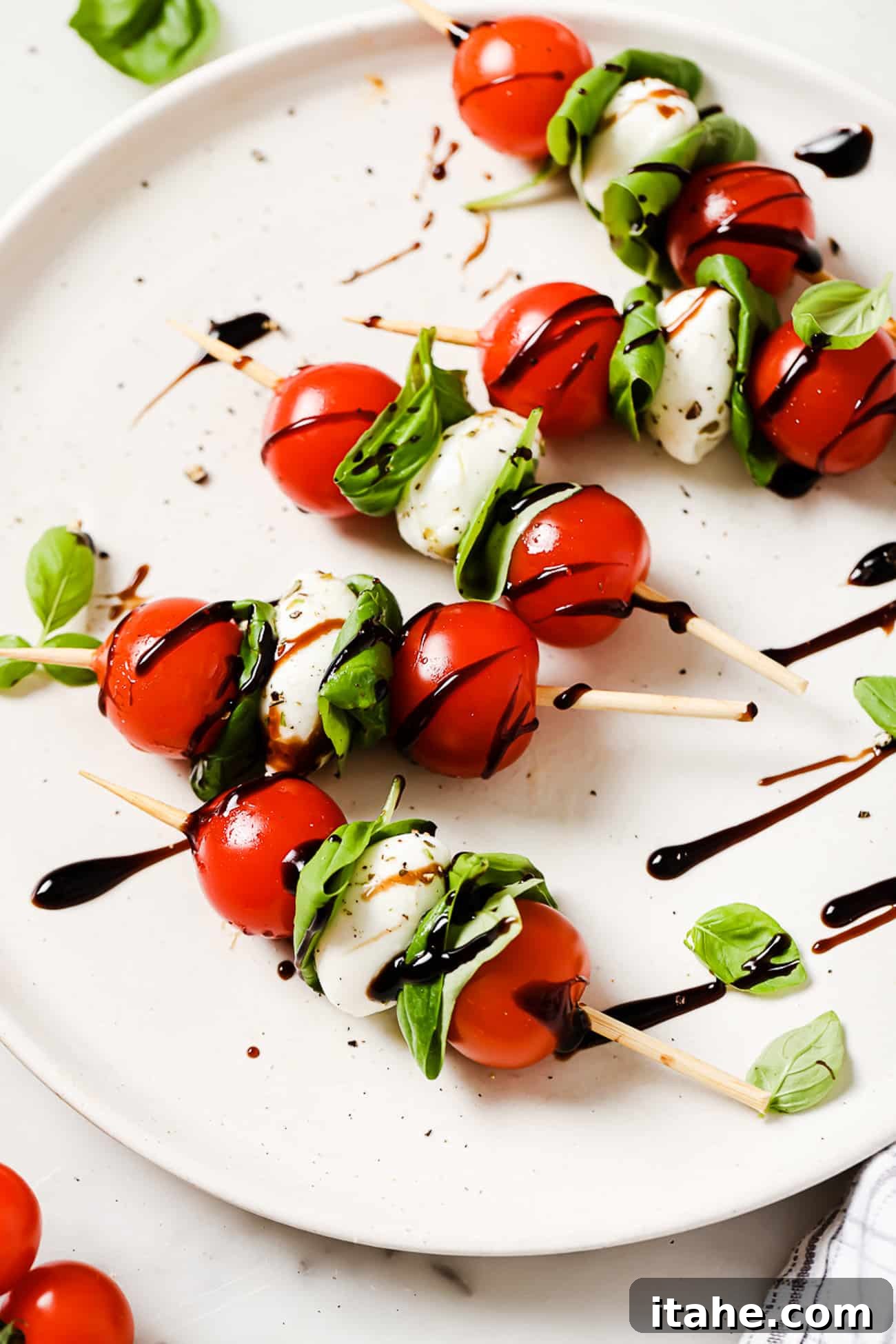 Caprese skewers drizzled with balsamic reduction on a white plate.