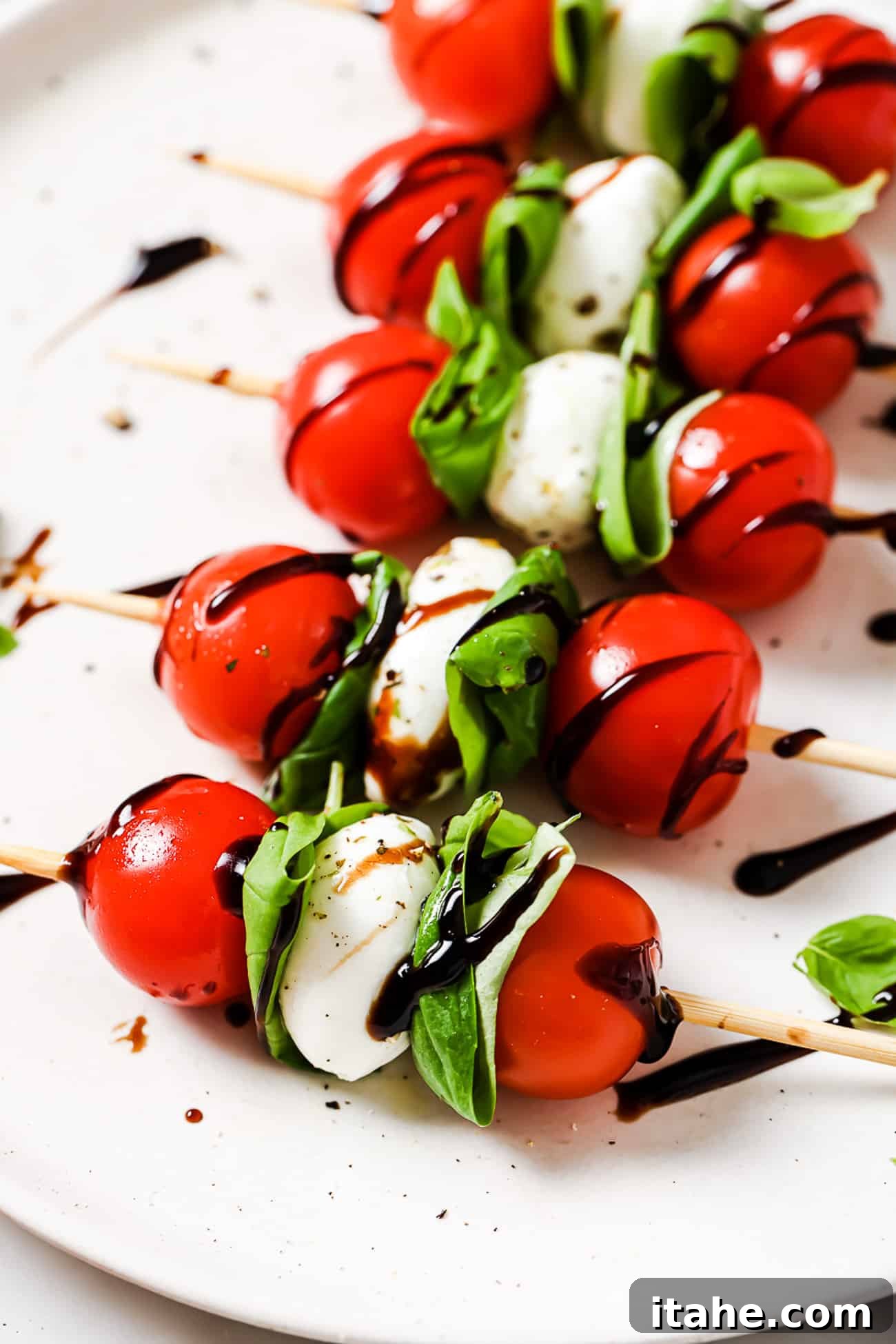 Caprese skewers with balsamic reduction on a white plate.