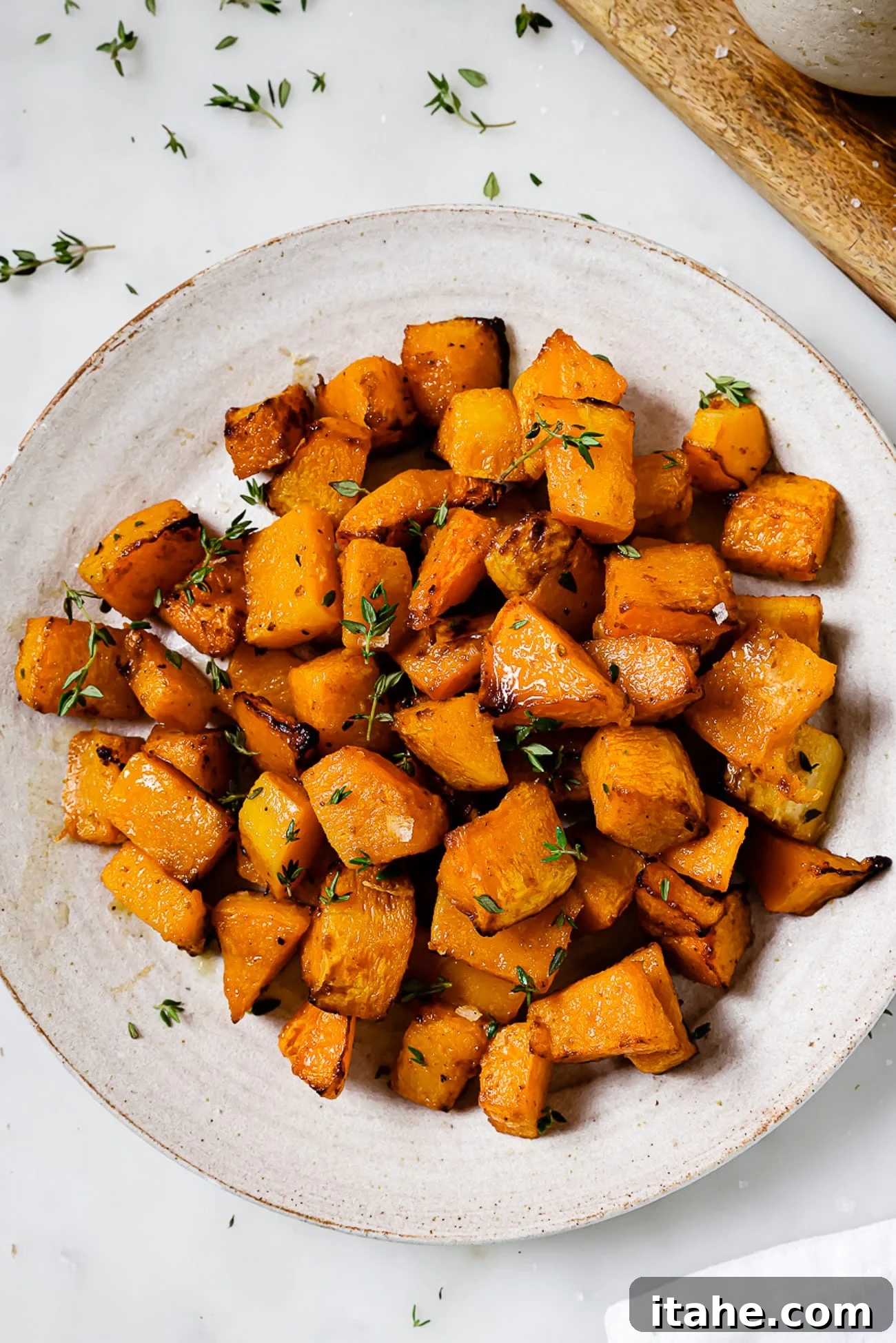 A serving platter of air fryer butternut squash garnished with thyme, showcasing its golden, caramelized edges.