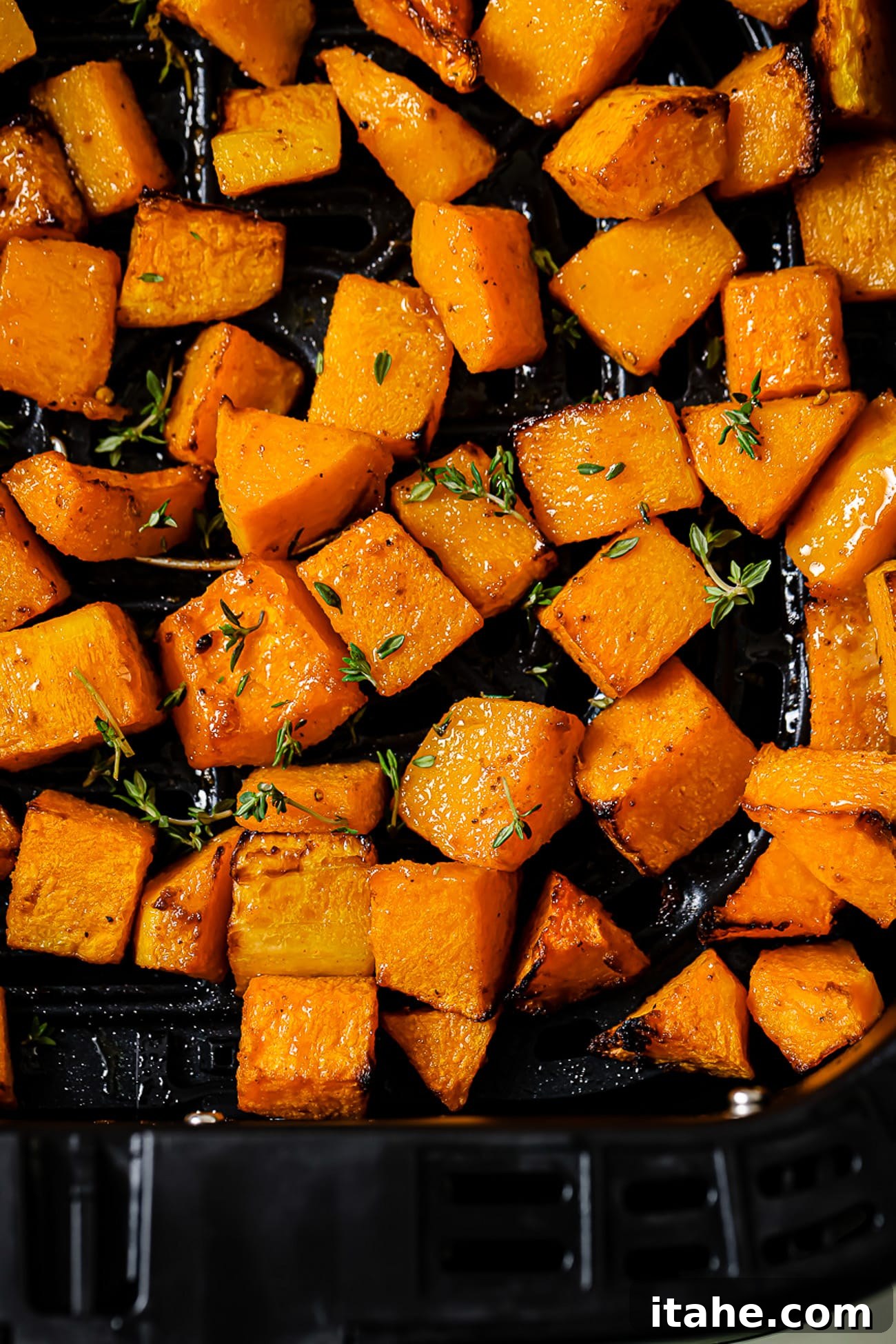 A close up of air fryer butternut squash topped with fresh thyme, emphasizing its perfect texture and appealing presentation.
