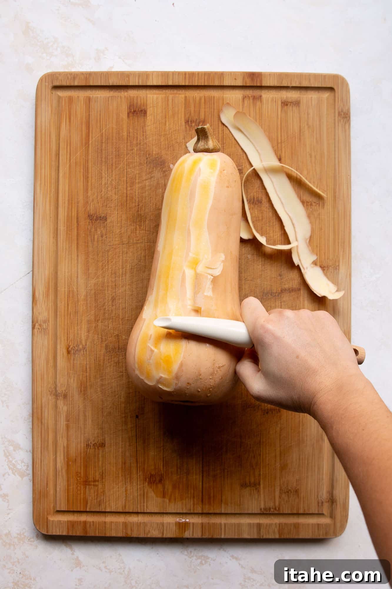 Someone expertly peeling butternut squash with a vegetable peeler, demonstrating the ease of skin removal.