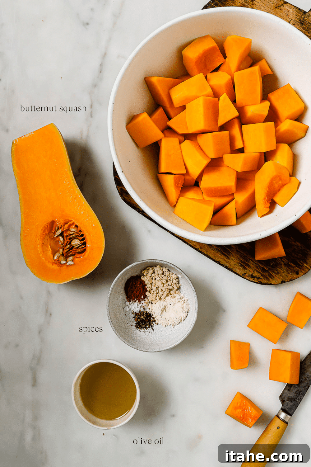 An overhead view of prepped ingredients and spices on a white countertop, including diced butternut squash, olive oil, and various seasonings.