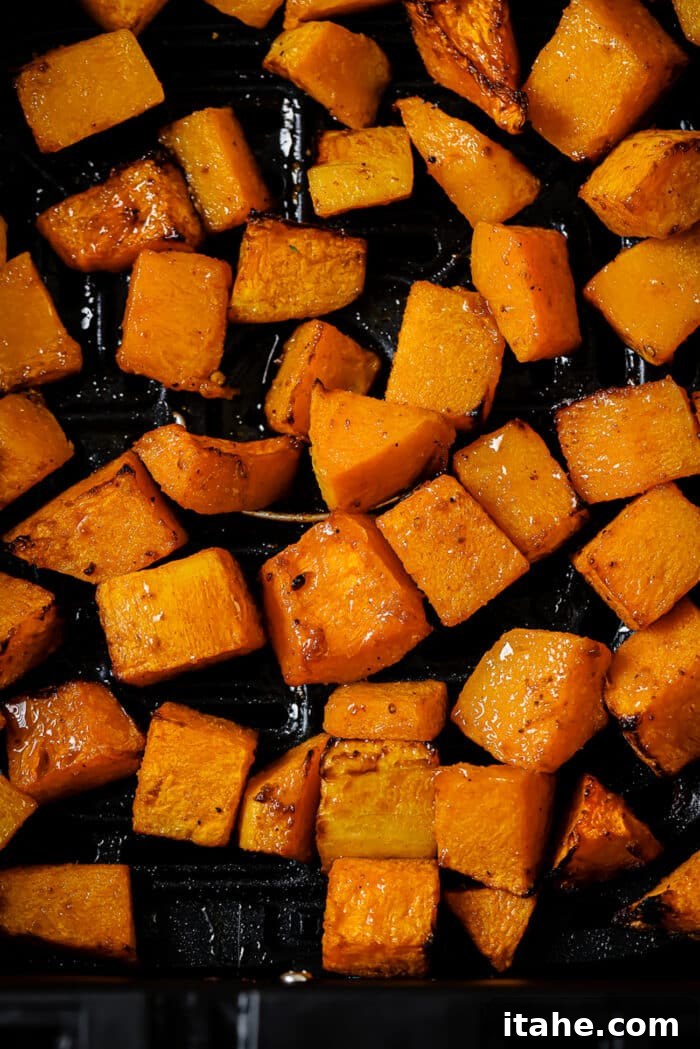 A close-up of beautifully golden and tender air fryer butternut squash in the air fryer basket, garnished with fresh herbs.