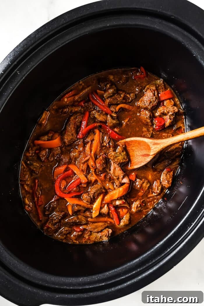 Slow Cooked Tender Pepper Steak 7 An overhead view of pepper steak, beef, and vegetables in a slow cooker, covered in sauce.