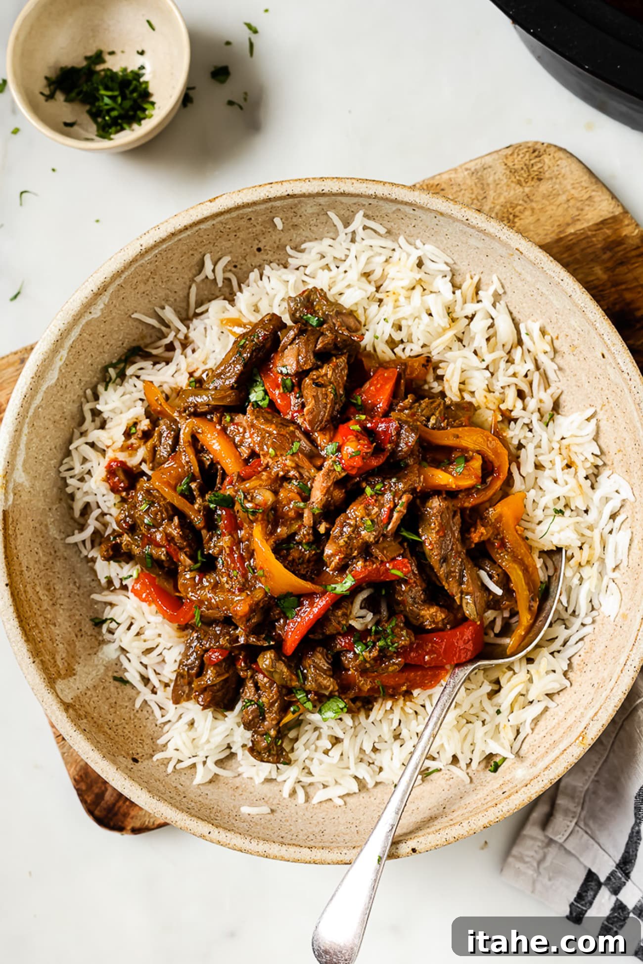 Slow Cooked Tender Pepper Steak 8 An overhead view of slow cooker pepper steak served over a bed of white rice, garnished for serving.