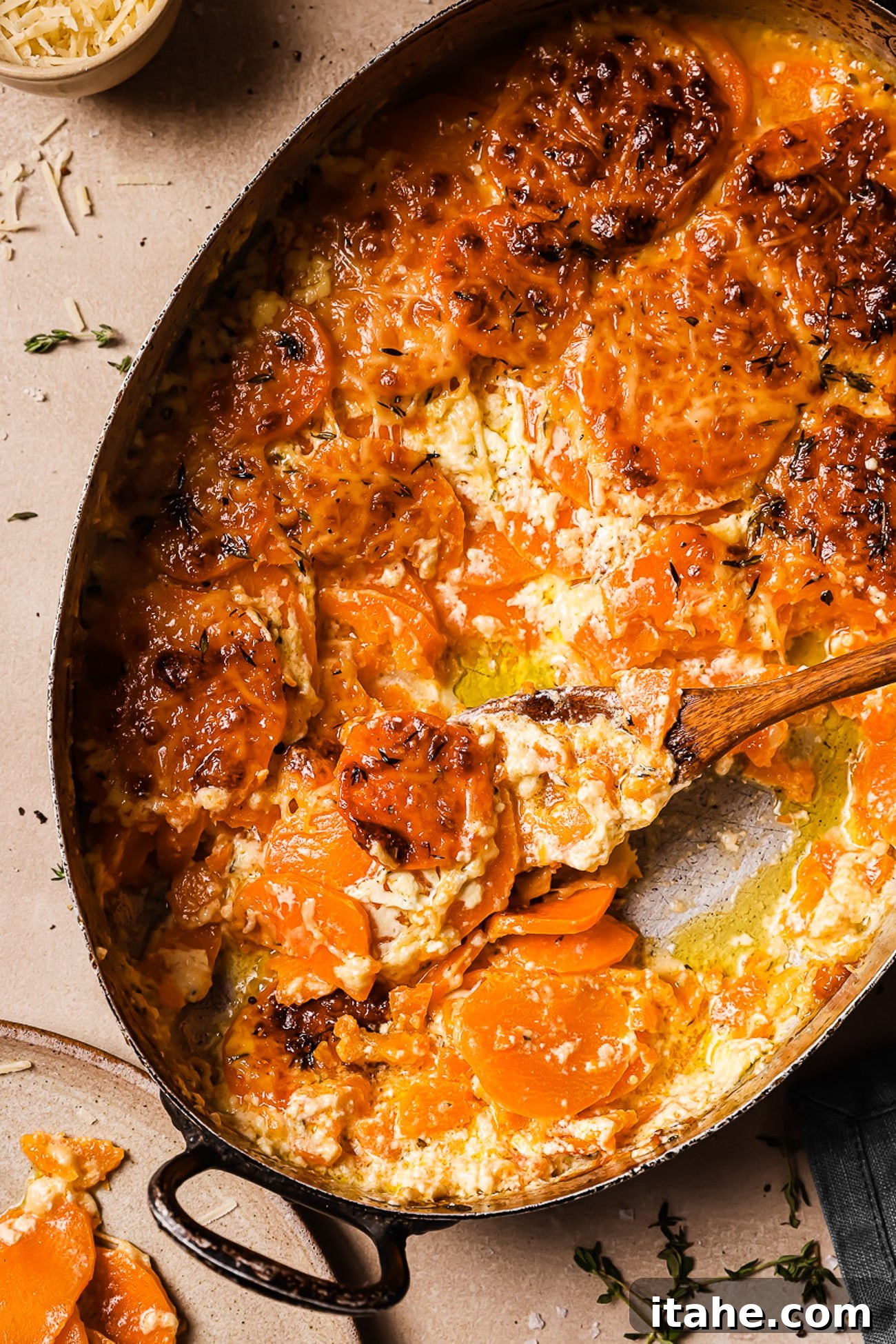 An overhead view of sweet potato gratin with a wooden spoon in it, ready to be served.