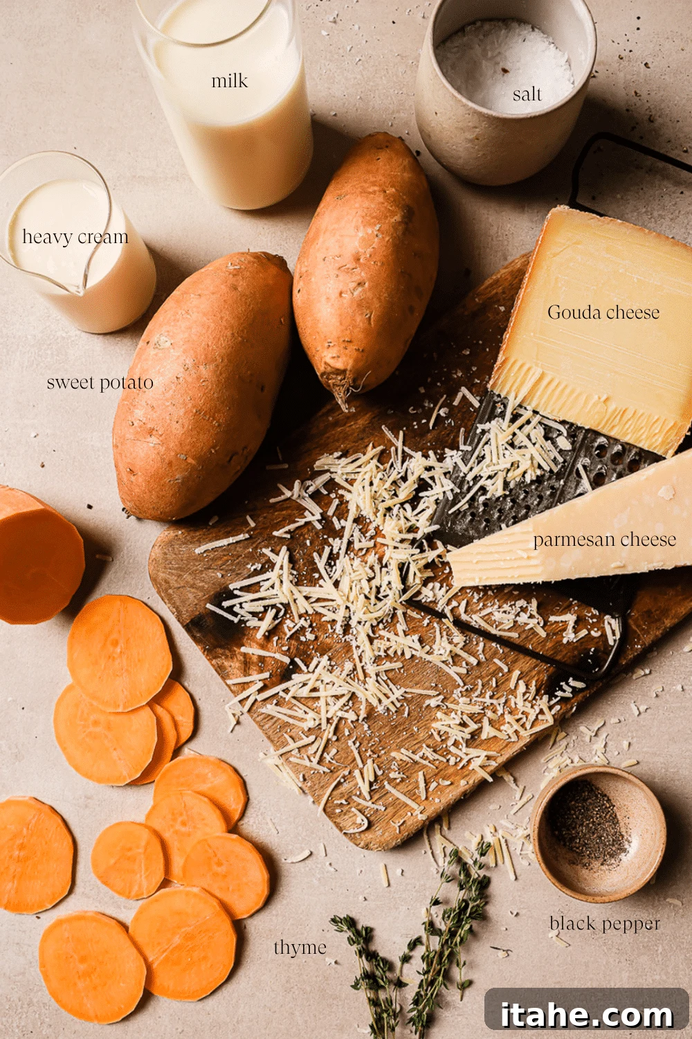 An overhead view of prepped ingredients on a wooden cutting board, including thinly sliced sweet potatoes, grated cheese, milk, cream, and fresh thyme.