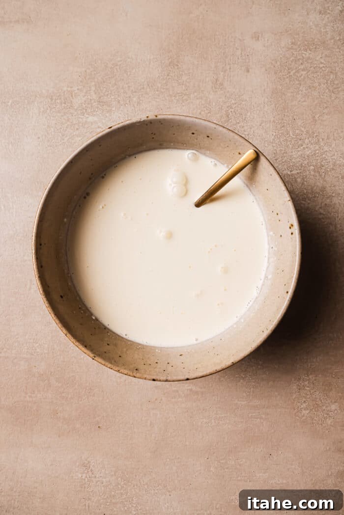 A bowl of milk and heavy cream with a spoon in it, ready to be combined.
