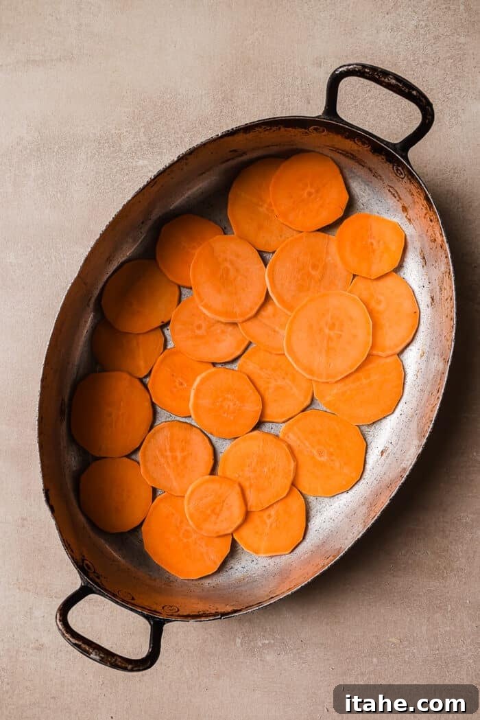 An overhead view of thinly sliced sweet potatoes in a baking pan, arranged in a single, even layer.