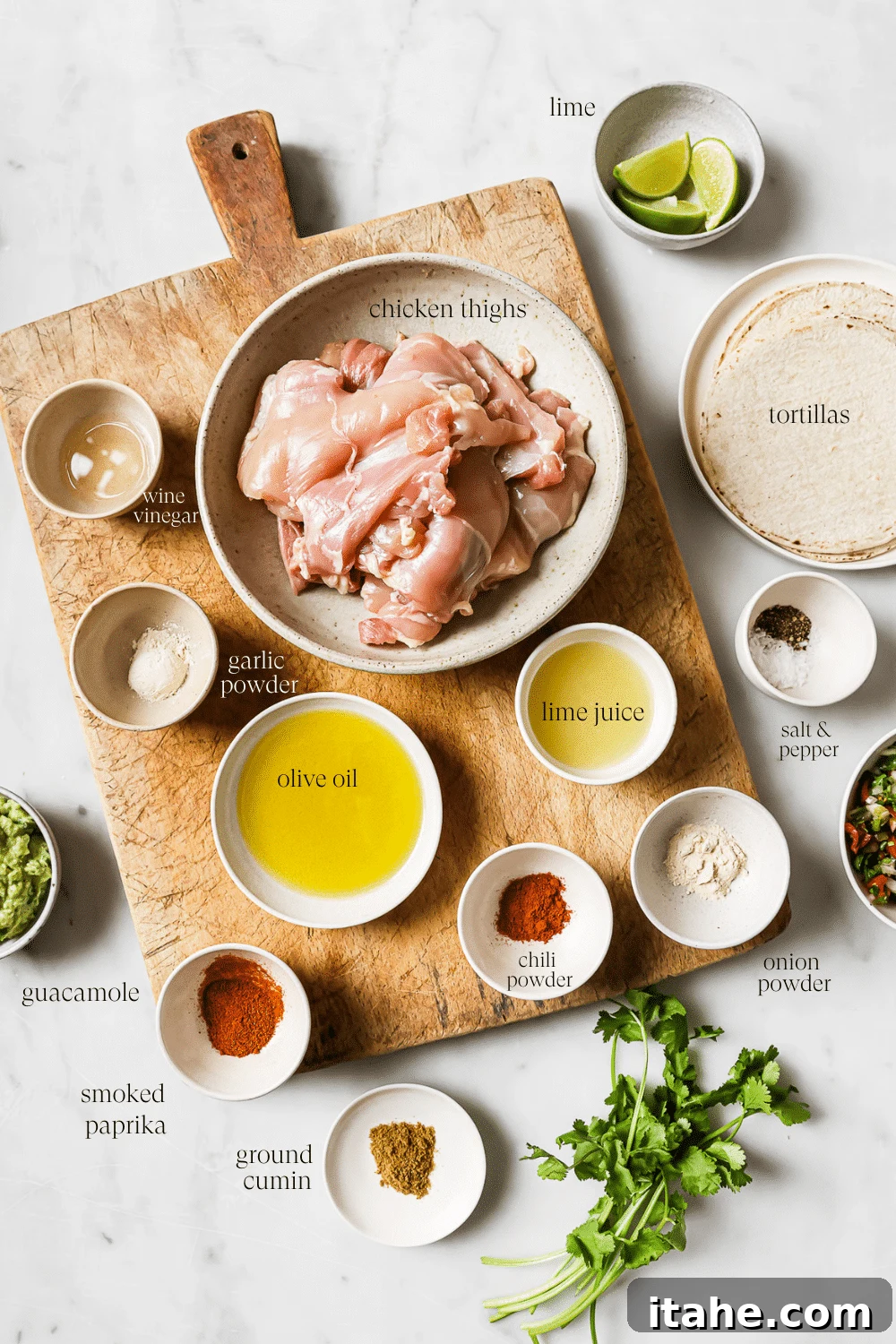 Assorted bowls of prepped ingredients for chicken tacos, neatly arranged on a rustic wooden cutting board and a clean white countertop.