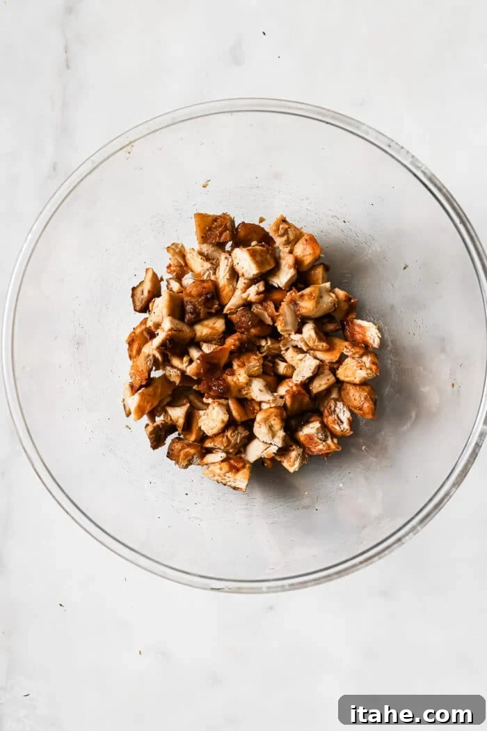 Perfectly cooked and diced chicken thighs, glistening and ready for taco assembly, displayed in a clear bowl on a white countertop.