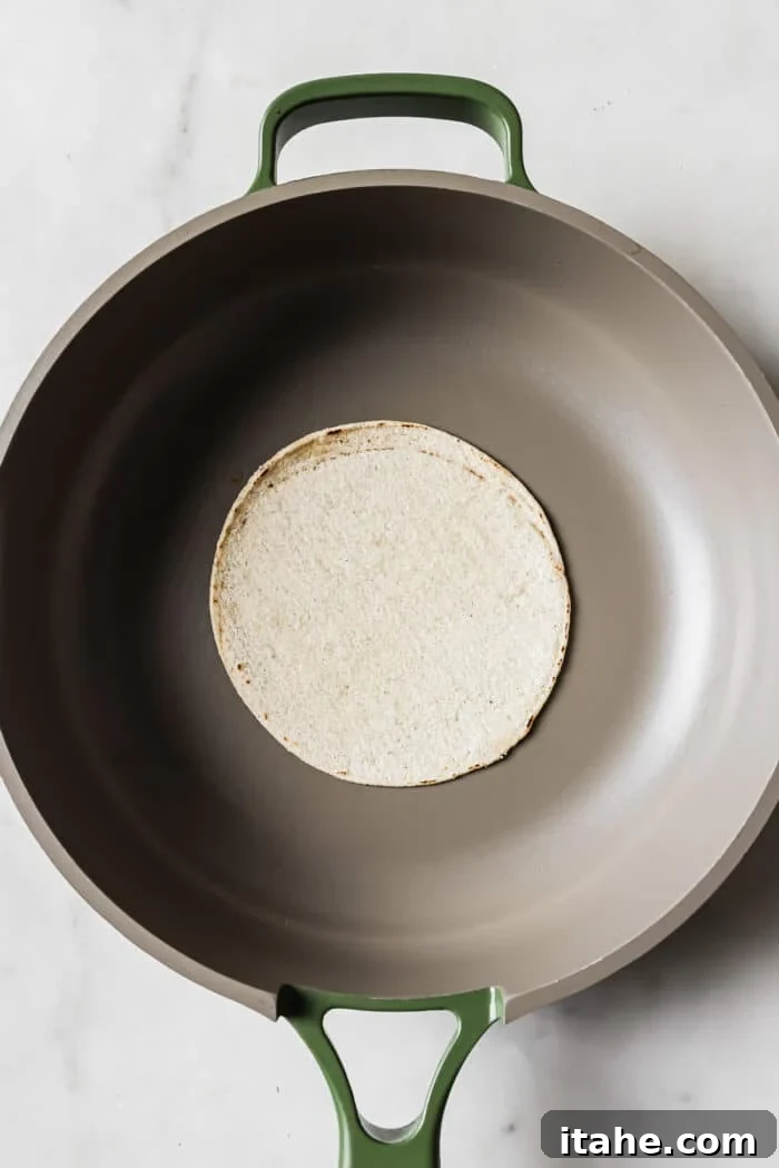 A single corn tortilla gently warming in the center of a large skillet, softening and preparing for its delicious taco filling.