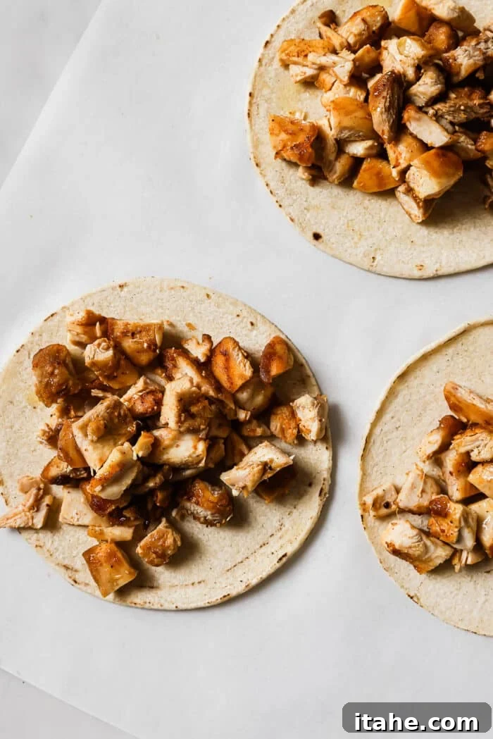 Warm corn tortillas generously piled with freshly diced, seasoned chicken, forming the base of a delicious taco, awaiting additional toppings.