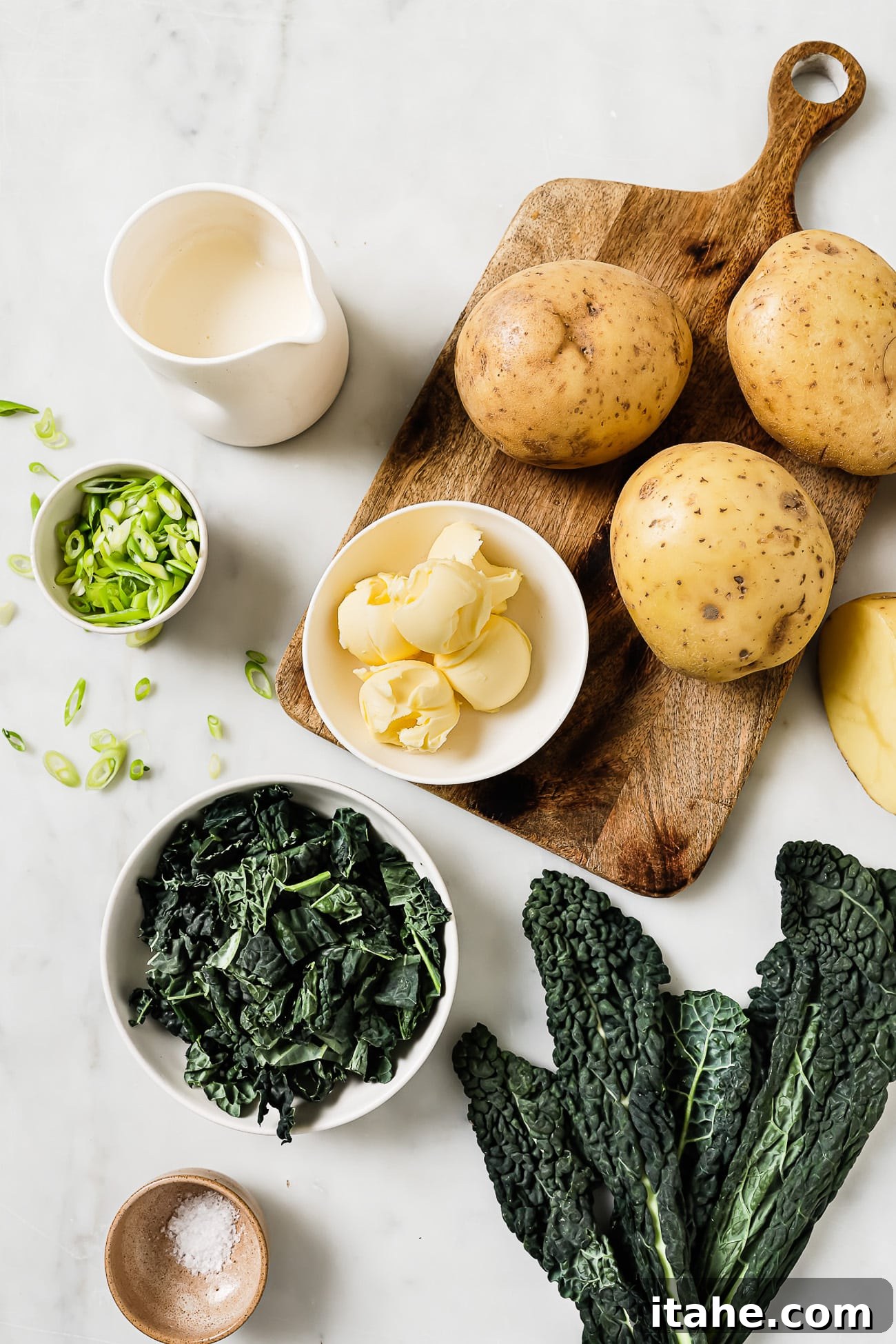 Colcannon ingredients in small bowls on a wooden cutting board and white countertop. 