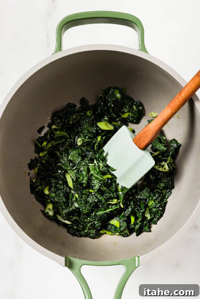 Wilted kale and green onions in a skillet on a white countertop. 