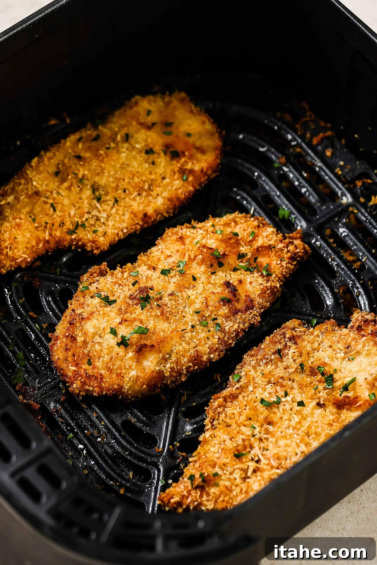 Three breaded chicken cutlets in an air fryer basket, perfectly golden brown and crispy.