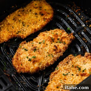 Air Fryer Chicken Cutlets on a white plate with lemon wedges and parsley.