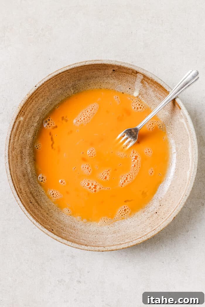 An overhead view of eggs beaten in a mixing bowl with a fork resting on the side of it.