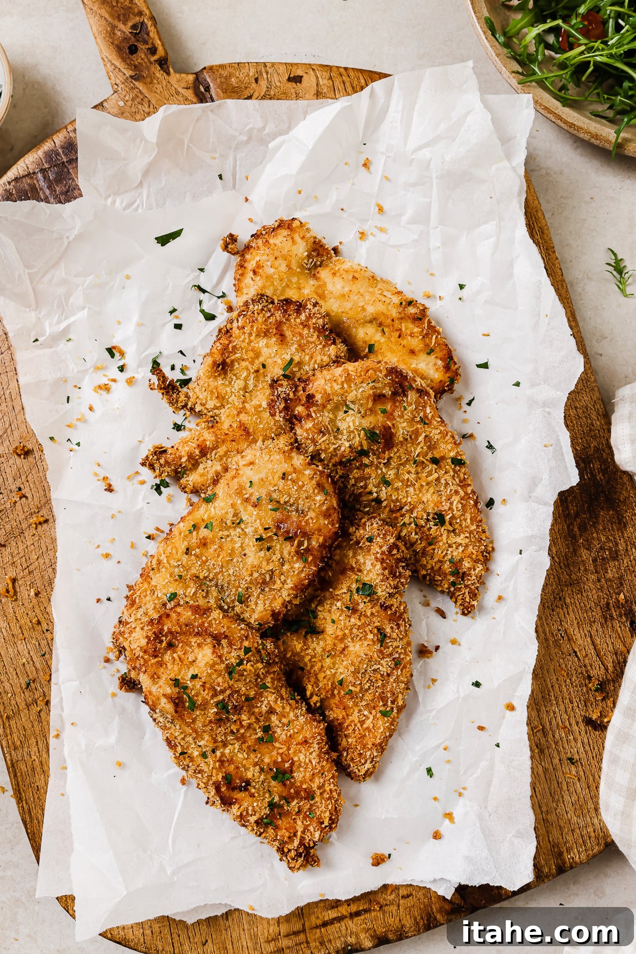 An overhead view of air fryer chicken cutlets resting on parchment paper on a cutting board, ready for serving.