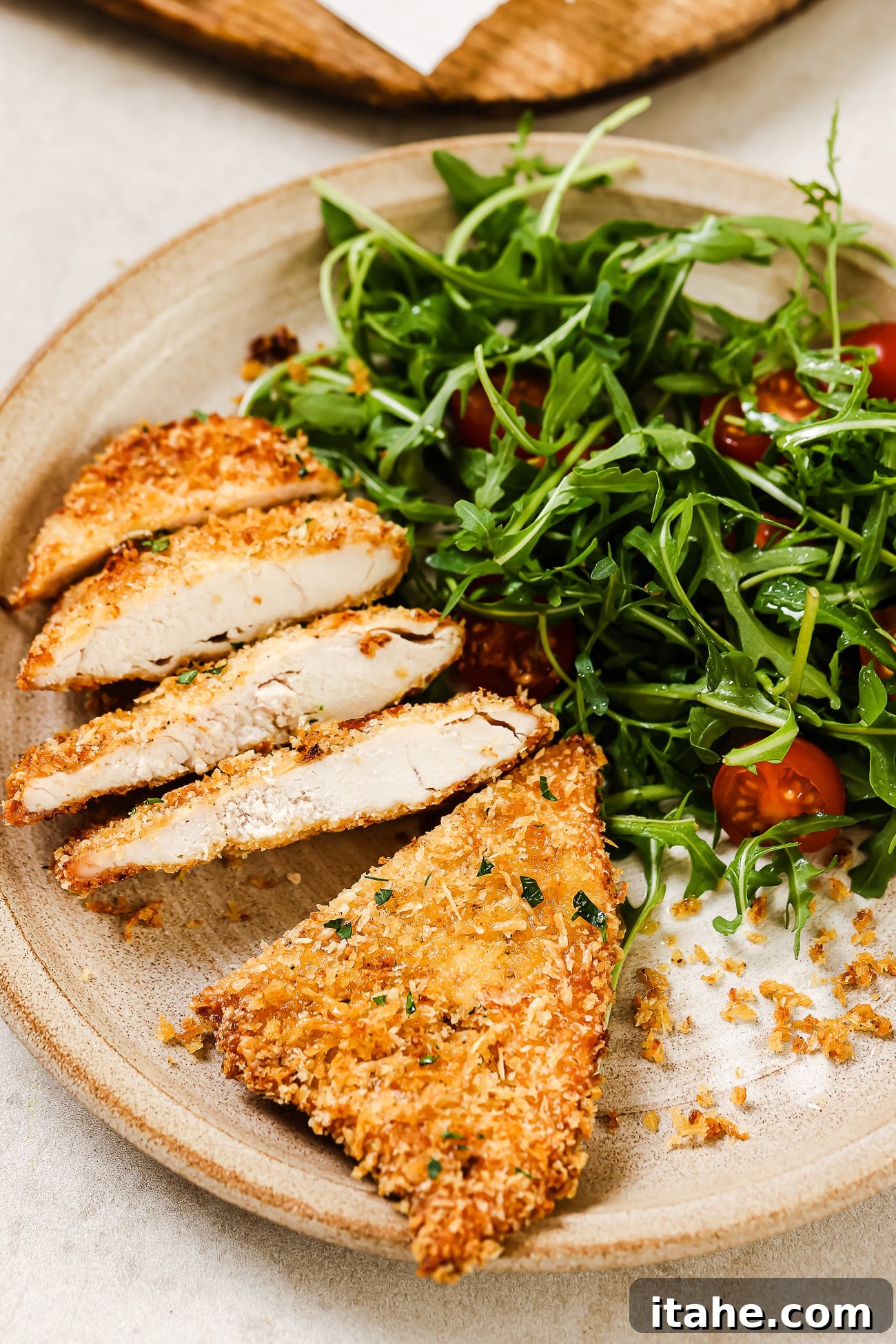 A perfectly sliced air fryer chicken cutlet on a plate with a fresh side salad, showcasing its juicy interior and crispy exterior.