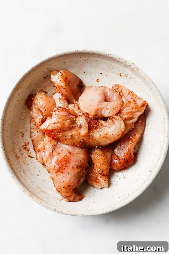 An overhead view of seasoned chicken tenders in a large mixing bowl, ready for cooking.