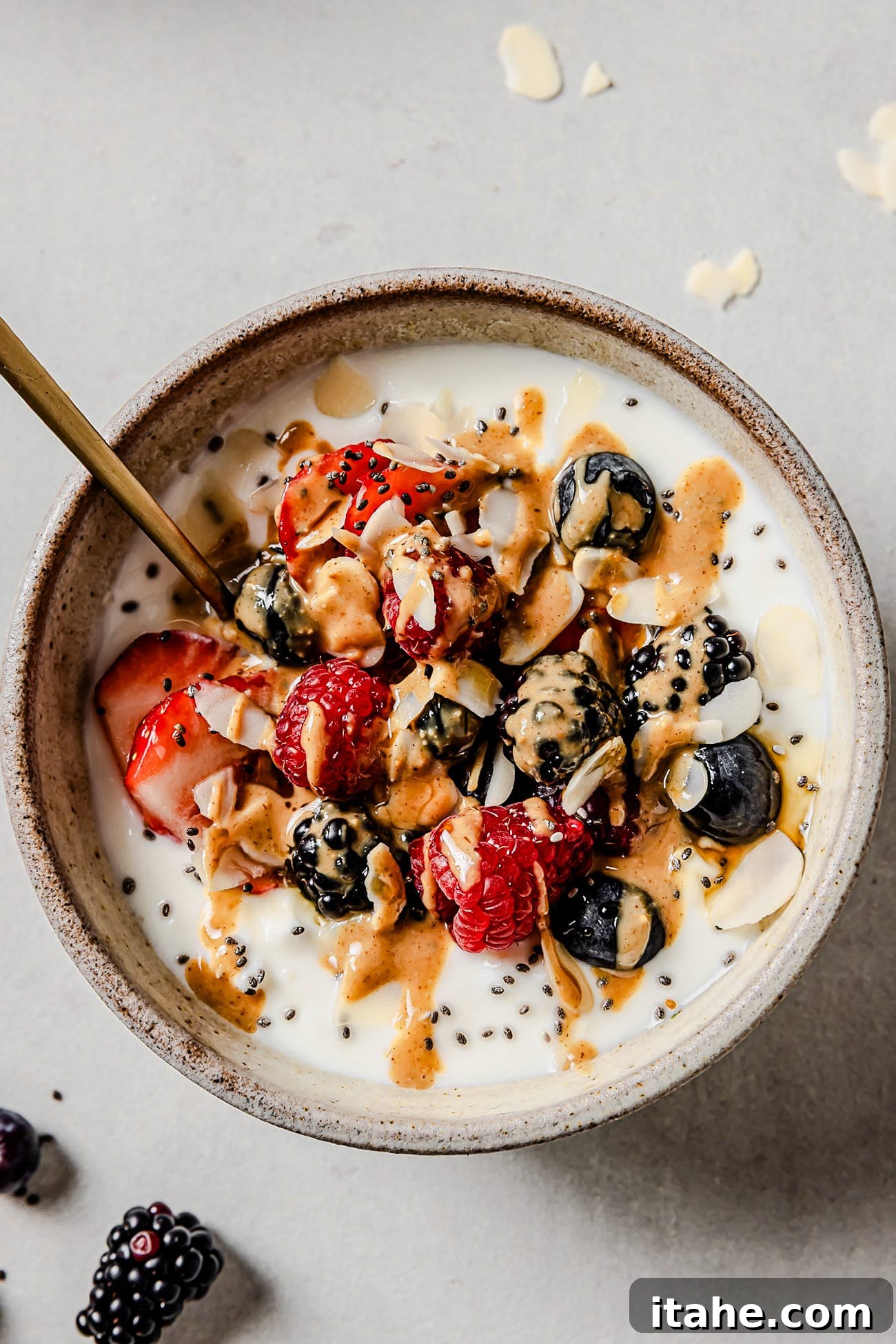 A beautifully arranged cottage cheese breakfast bowl topped with mixed berries, chia seeds, a generous drizzle of maple syrup, and a swirl of creamy peanut butter.