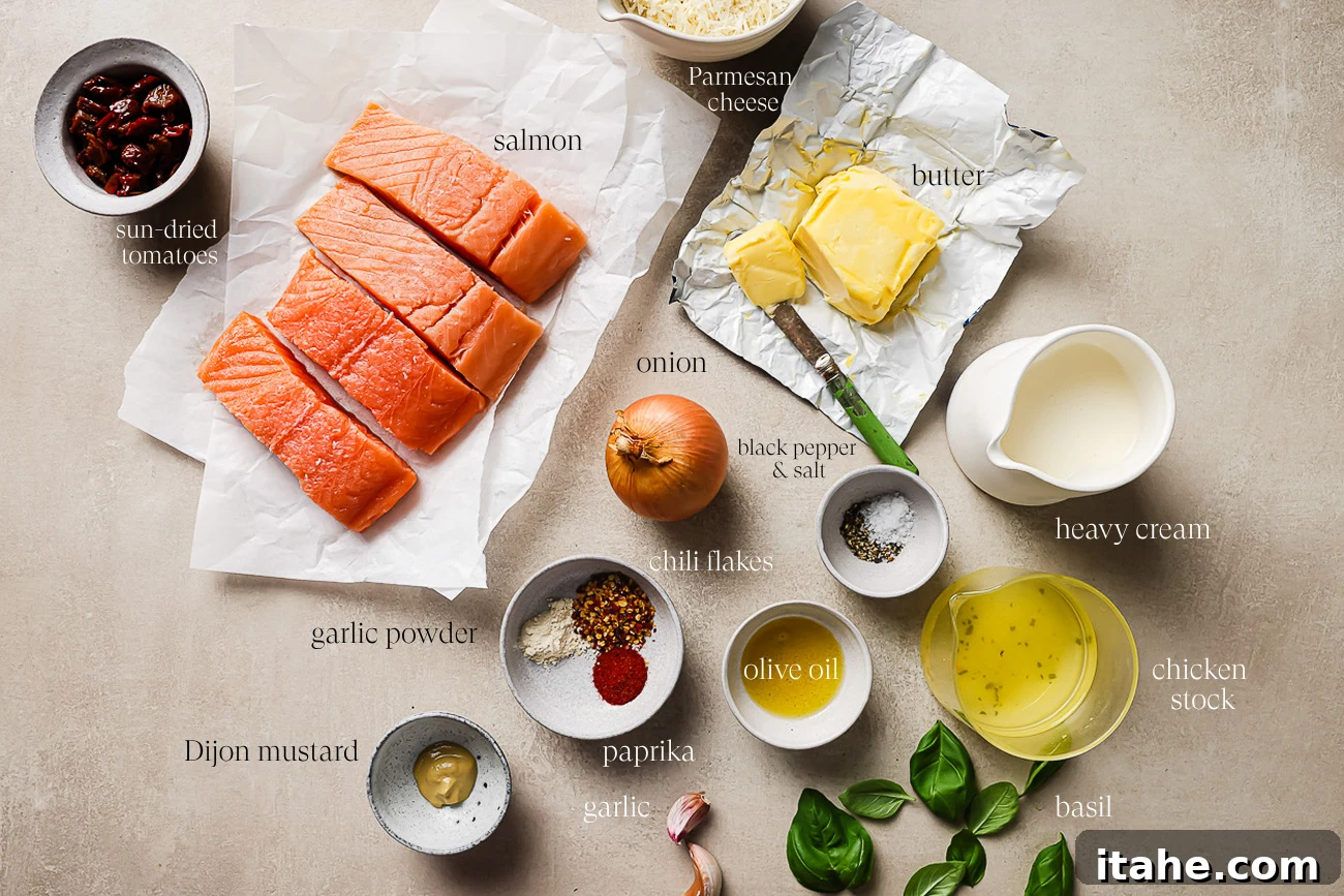 Collection of key ingredients on a kitchen countertop, including salmon fillets, various spices, a yellow onion, garlic cloves, chicken broth, heavy cream, Dijon mustard, Parmesan cheese, sun-dried tomatoes, and fresh basil.