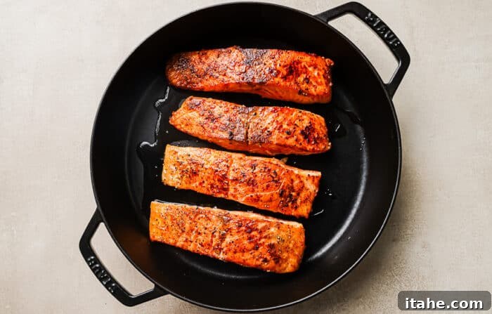 Seared salmon fillets cooking in a cast-iron skillet, achieving a golden-brown crust.