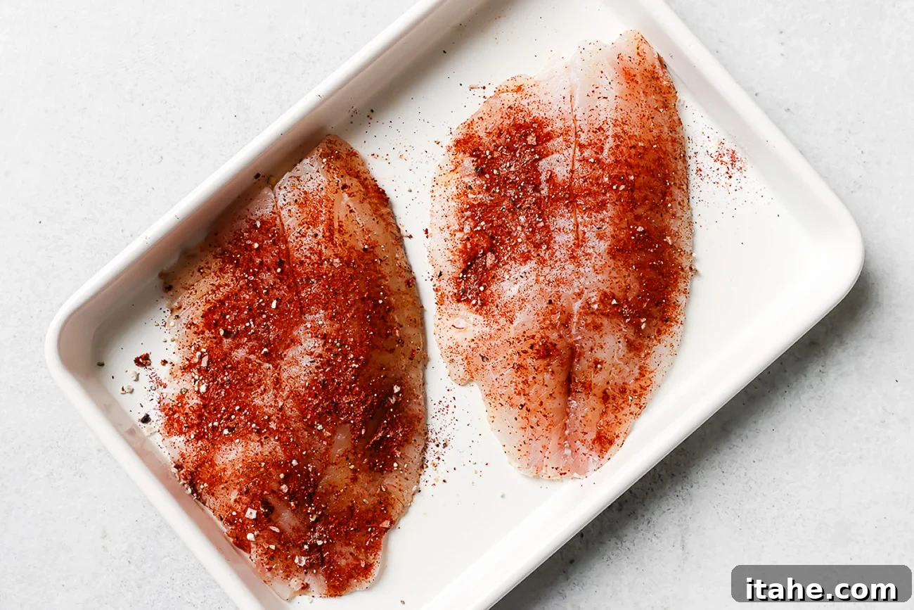 Seasoned raw tilapia fillet on a white baking sheet.