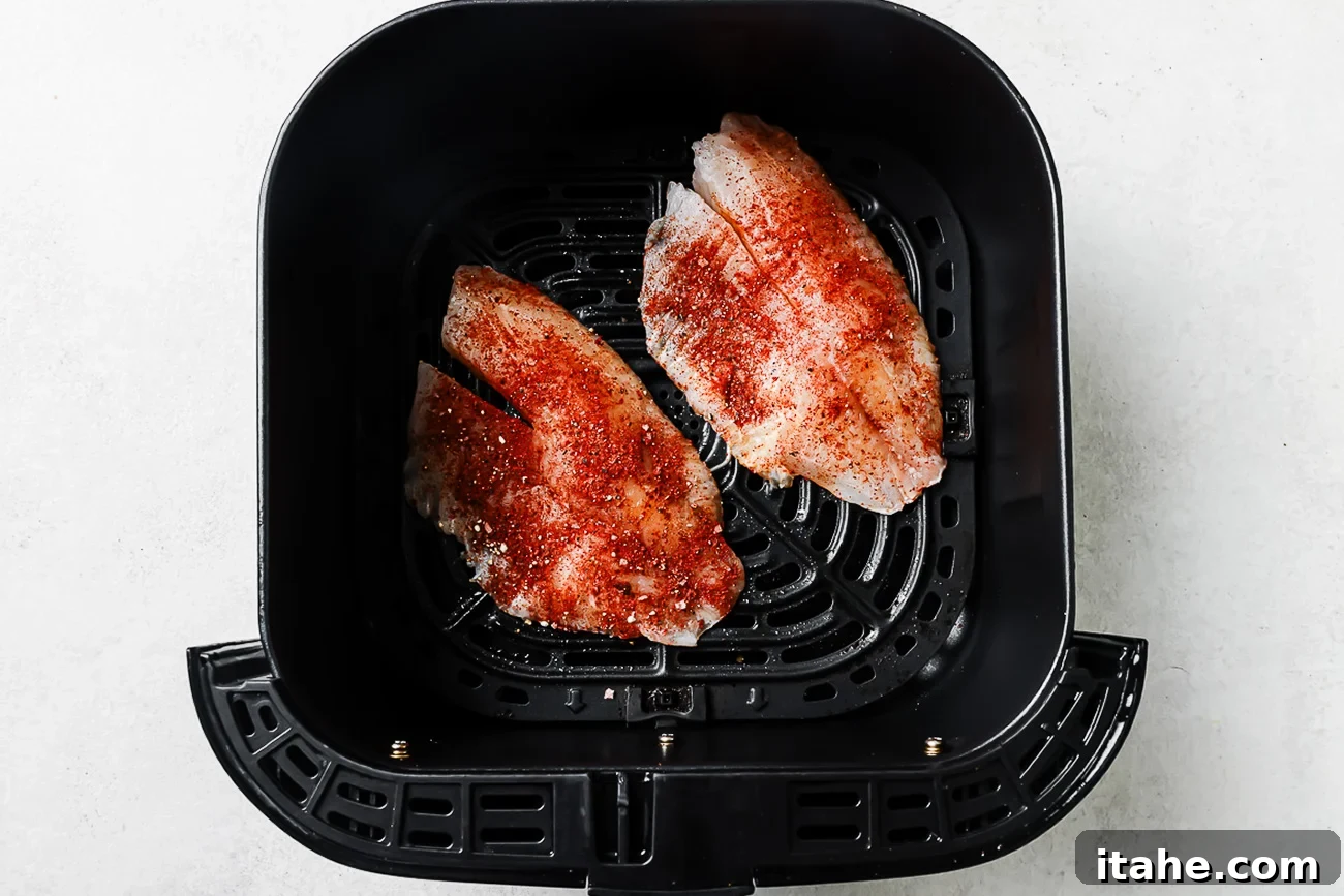 Seasoned raw tilapia in an air fryer basket.