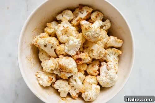 Seasoned raw cauliflower florets in a bowl, ready for air frying.
