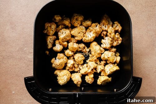 Cauliflower florets arranged in a single layer in an air fryer basket.