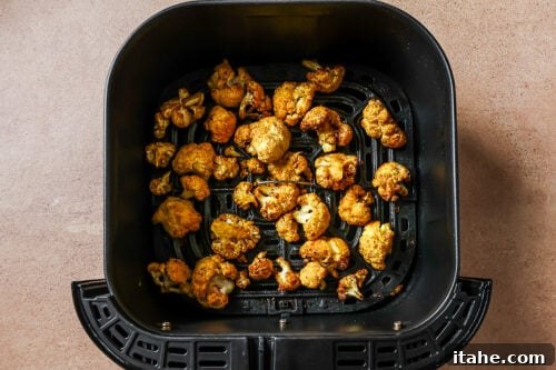 Cooked, golden-brown cauliflower florets in an air fryer basket after cooking.