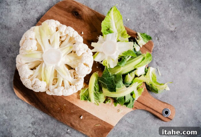 Crispy Roasted Air Fryer Cauliflower 4 Whole cauliflower head on a wooden cutting board, with green leaves visible.