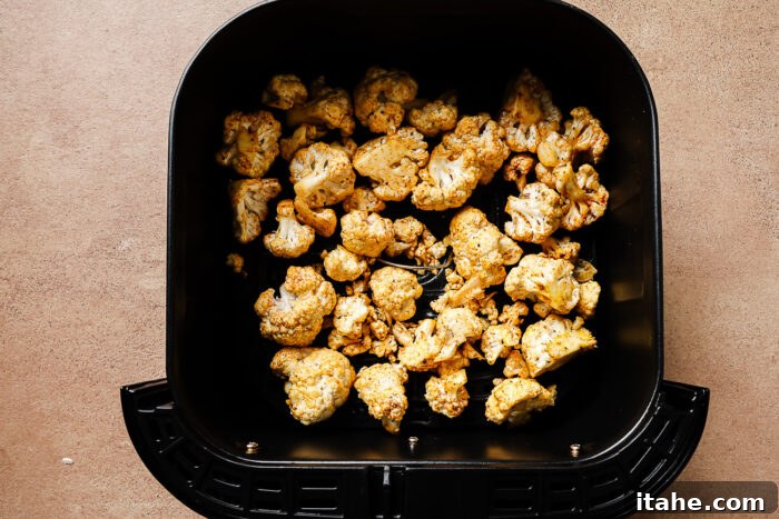 Crispy Roasted Air Fryer Cauliflower 9 Overhead view of raw cauliflower florets seasoned with spices in an air fryer basket.