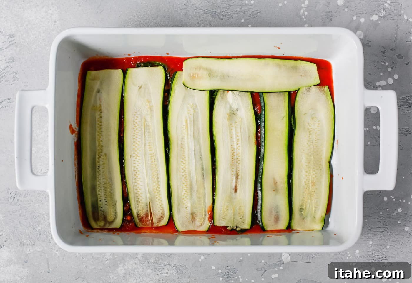 Noodle-Free Zucchini Lasagna 4 Overhead view of a white casserole dish showing zucchini slices neatly layered over the tomato sauce.