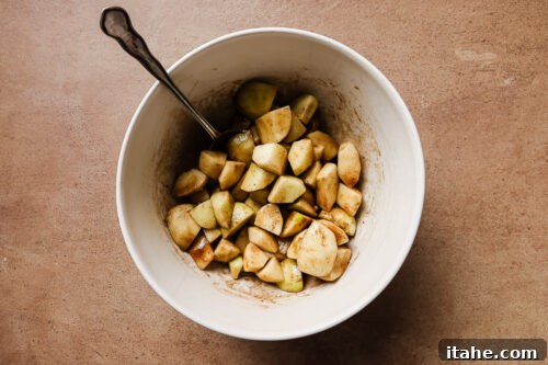 Diced and peeled apples mixed with warm spices in a white bowl, ready for baking.