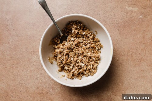 Almond flour, rolled oats, and sugar mixed in a white bowl to create a crunchy apple crisp topping.