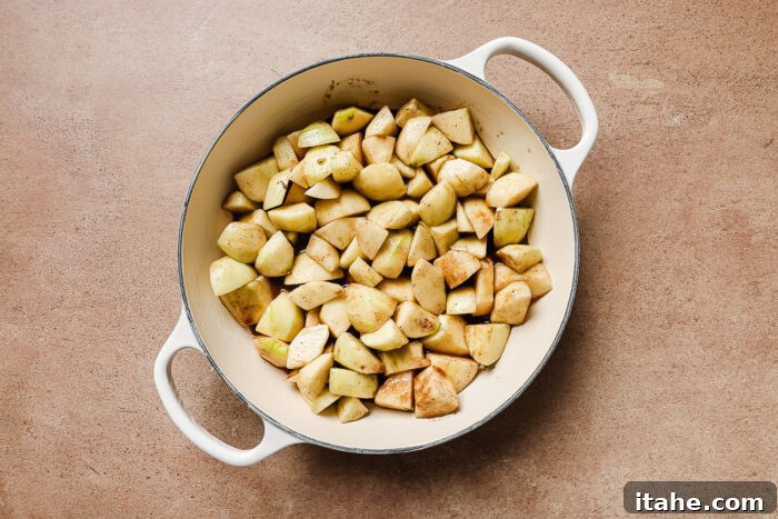 Diced and peeled apples mixed with warm spices in a white skillet, ready for baking.