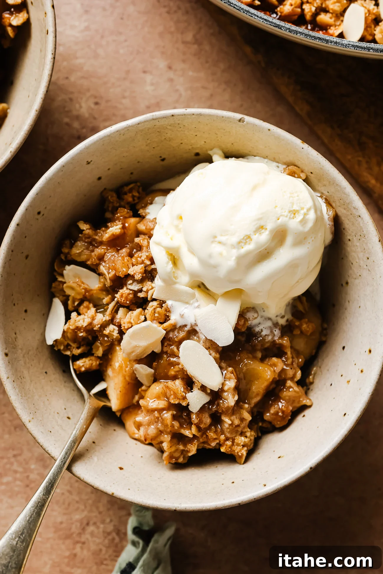 Gluten-free apple crisp in a white bowl topped with creamy vanilla ice cream for a cozy dessert.