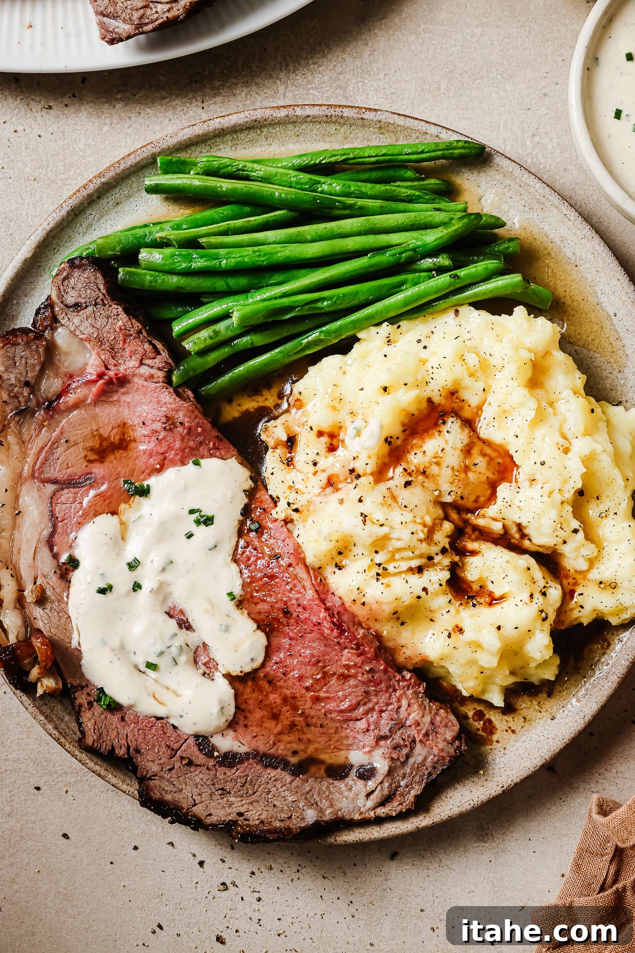 Juicy slices of reverse sear prime rib served with mashed potatoes, green beans, and horseradish sauce on a plate. A perfect holiday dinner.