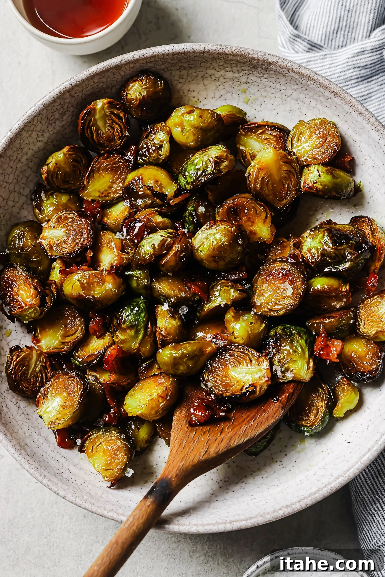 Caramelized Maple Bacon Brussels Sprouts 2 Overhead view of maple bacon Brussels sprouts in a white platter, coated in a sweet maple glaze with crispy bacon pieces.
