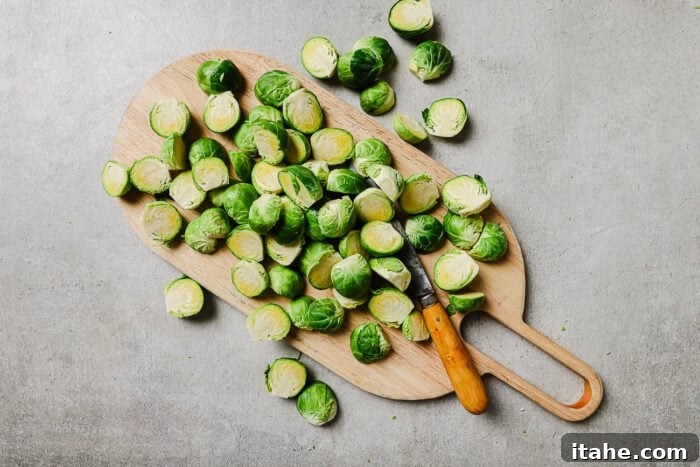Caramelized Maple Bacon Brussels Sprouts 4 Fresh Brussels sprouts halved on a wooden cutting board with a knife, ready to be roasted.